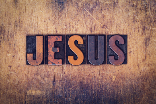 The word "Jesus" written in dirty vintage letterpress type on a aged wooden background.